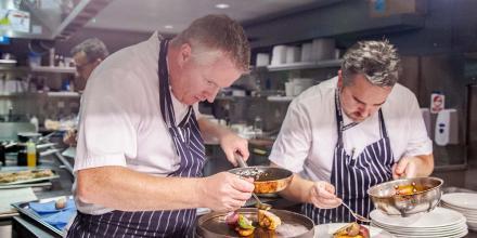 two chefs working together on the final plating of a gourmet dish