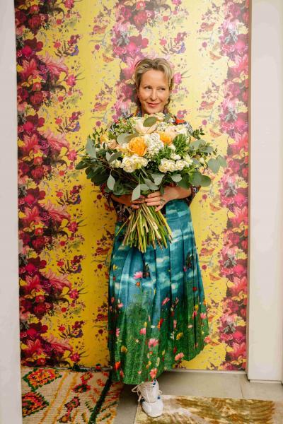 Nikki Tibbles stood with a colourful bouquet of fresh flowers against a red and gold backdrop